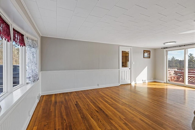 unfurnished room with wood finished floors and a wainscoted wall