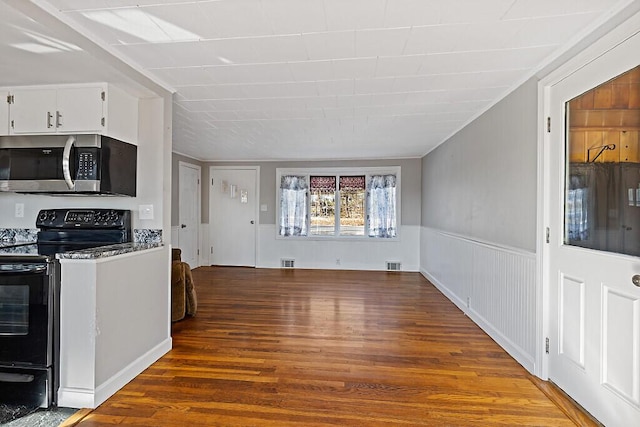 kitchen featuring visible vents, stainless steel microwave, white cabinetry, wood finished floors, and black range with electric stovetop