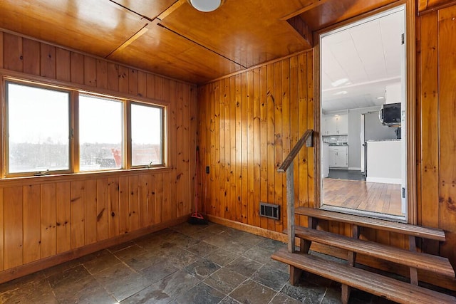 unfurnished room with stone finish flooring, visible vents, wood ceiling, wood walls, and baseboards