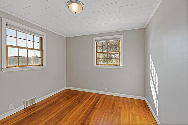 empty room featuring crown molding, visible vents, baseboards, and wood finished floors