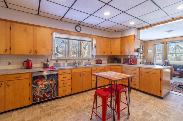 kitchen with dishwasher, a sink, stainless steel countertops, a peninsula, and a drop ceiling