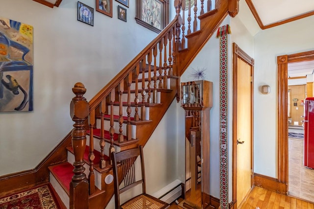 stairway with baseboards, a baseboard heating unit, ornamental molding, and wood finished floors