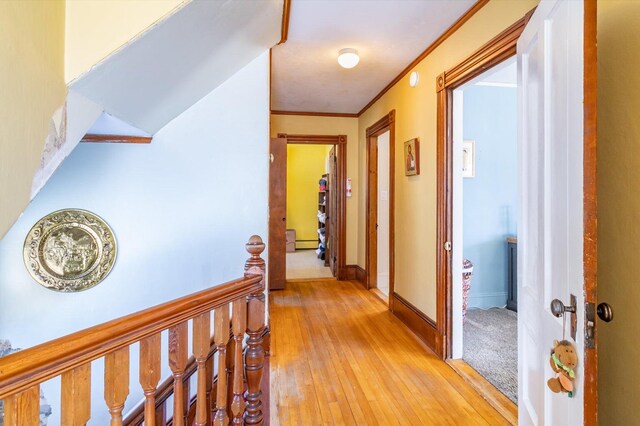 hall featuring baseboards, light wood-style flooring, a baseboard heating unit, and ornamental molding