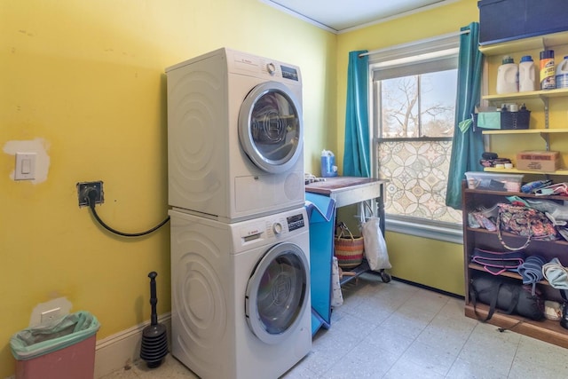 laundry room featuring stacked washer / dryer, laundry area, baseboards, and light floors
