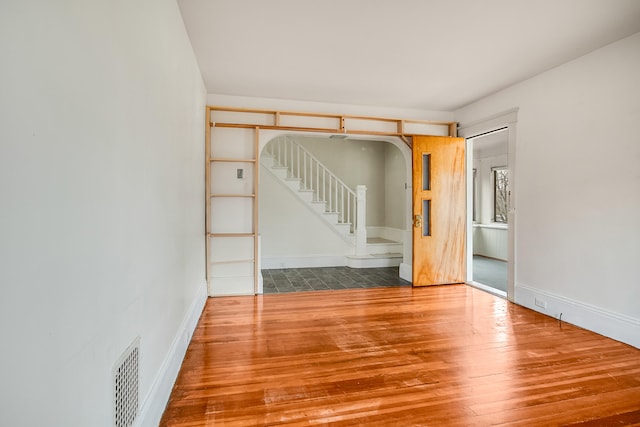 empty room with stairway, hardwood / wood-style floors, arched walkways, baseboards, and visible vents
