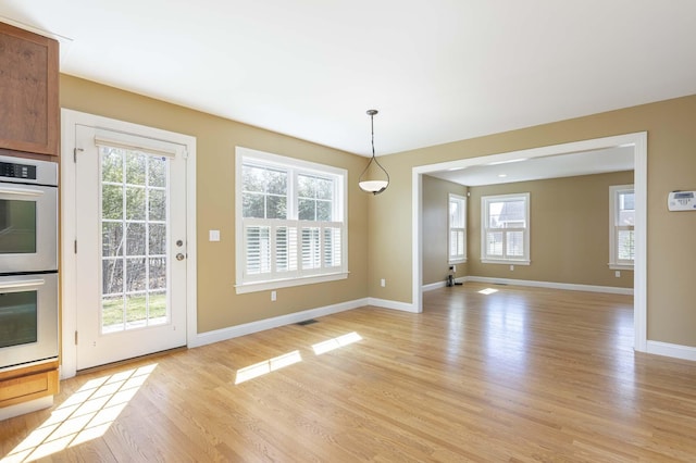 unfurnished dining area featuring a healthy amount of sunlight, light wood finished floors, and baseboards