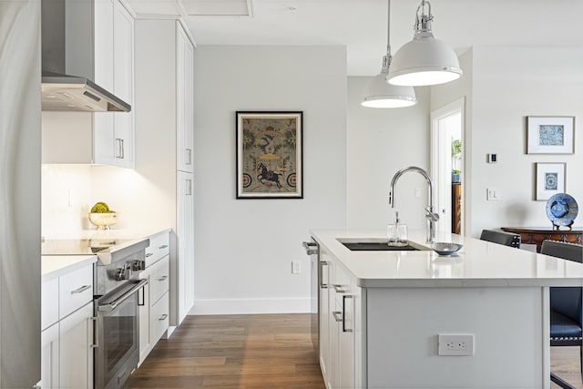 kitchen featuring an island with sink, dark wood-style floors, wall chimney exhaust hood, a sink, and stainless steel appliances