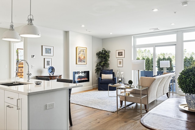 living room featuring recessed lighting, a glass covered fireplace, visible vents, and light wood-type flooring
