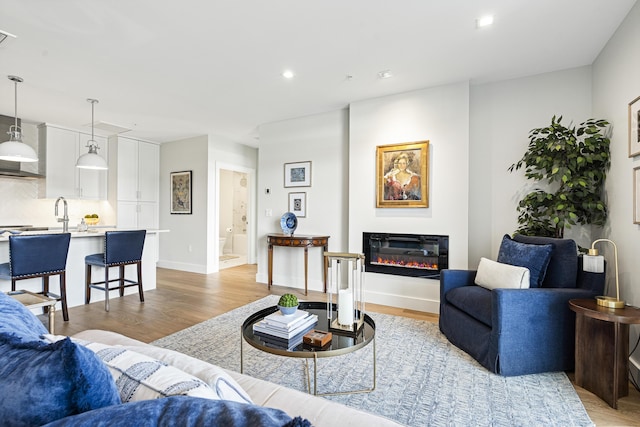 living area featuring recessed lighting, light wood-style flooring, a glass covered fireplace, and baseboards