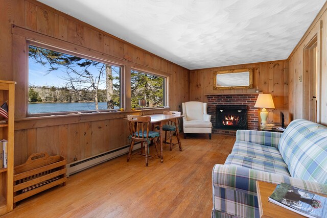 57 Samoset Trl, Boothbay, ME 04544 - living room with a water view, light wood-type flooring, baseboard heating, wood walls, and a fireplace