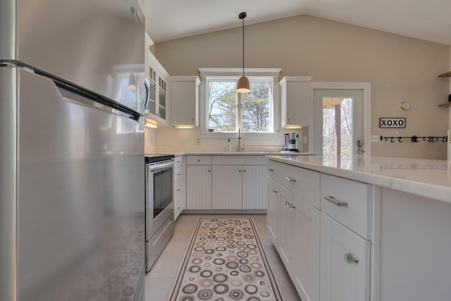 kitchen with appliances with stainless steel finishes, white cabinetry, lofted ceiling, pendant lighting, and decorative backsplash