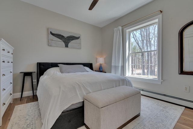 bedroom with light wood-style flooring, a baseboard heating unit, ceiling fan, and multiple windows