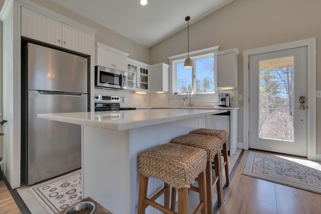 kitchen featuring light countertops, appliances with stainless steel finishes, a kitchen breakfast bar, a kitchen island, and lofted ceiling