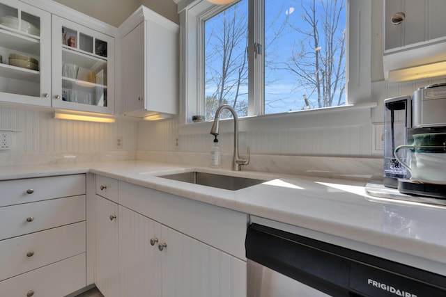 kitchen featuring white cabinets, a sink, glass insert cabinets, and dishwashing machine