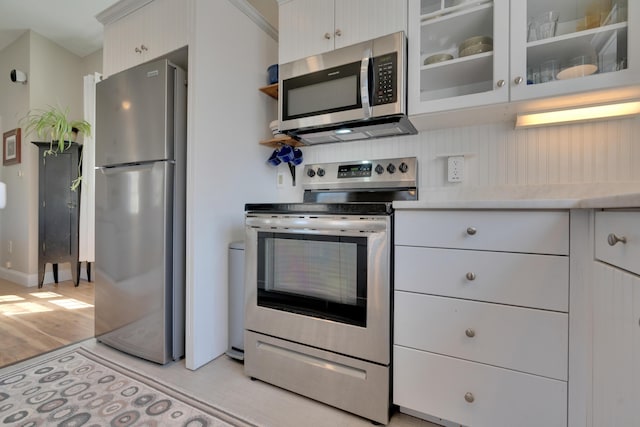 kitchen with glass insert cabinets, baseboards, light countertops, appliances with stainless steel finishes, and light wood-style flooring