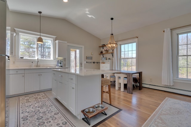 kitchen featuring vaulted ceiling, light countertops, white cabinets, light wood finished floors, and a sink