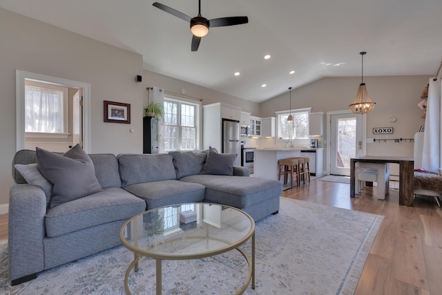 living room featuring light wood-style floors, ceiling fan with notable chandelier, lofted ceiling, and recessed lighting