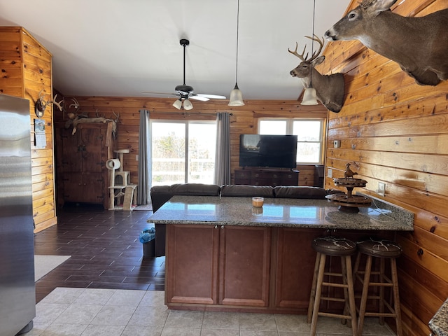 441 Works Rd, Jackson, ME 04921 - kitchen with dark stone countertops, freestanding refrigerator, a kitchen breakfast bar, wooden walls, and a ceiling fan