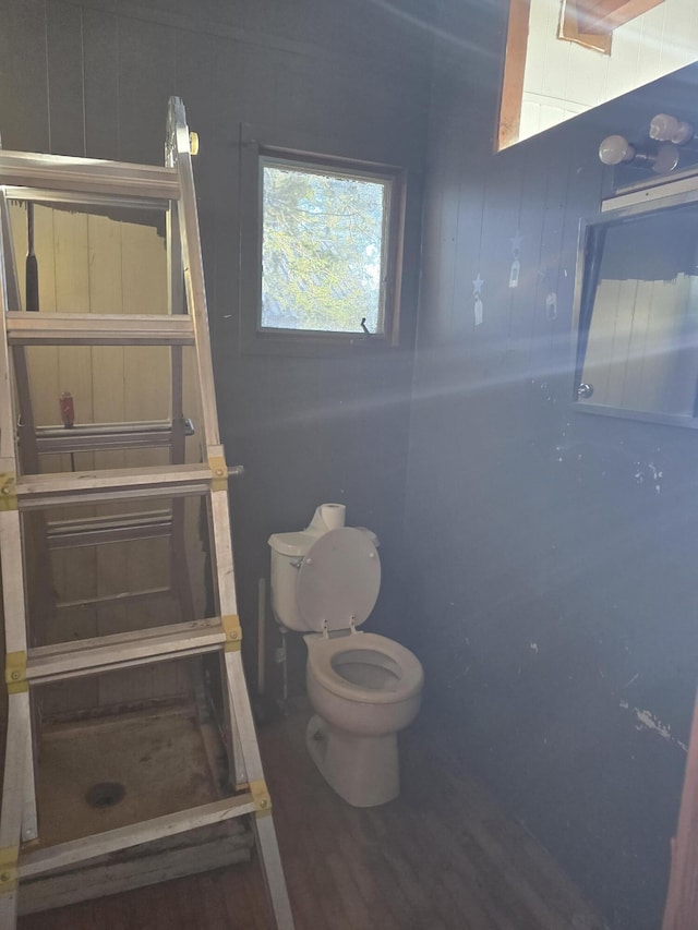 bathroom with toilet, tiled shower, and wood finished floors
