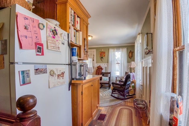27 Pine St, Eustis, ME 04936 - kitchen with freestanding refrigerator, crown molding, wood finished floors, wainscoting, and brown cabinets