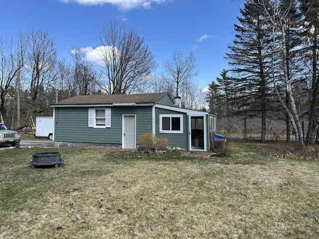rear view of property featuring a fire pit, a chimney, and a lawn