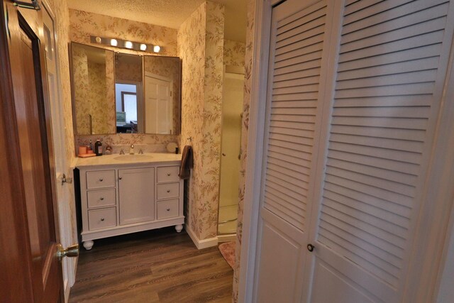 bathroom with a closet, baseboards, vanity, wood finished floors, and wallpapered walls