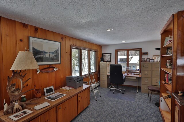 carpeted office space featuring wooden walls, plenty of natural light, and a textured ceiling