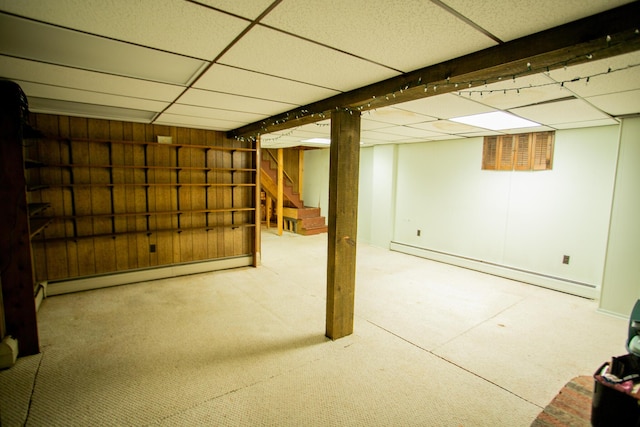 finished below grade area with baseboard heating, a baseboard heating unit, stairway, carpet floors, and a drop ceiling
