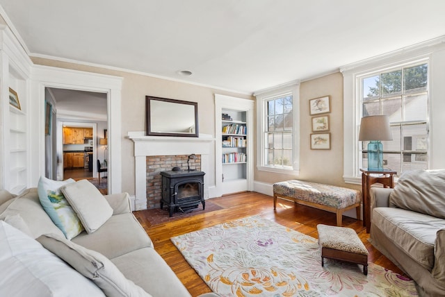 living area featuring wood finished floors, a wood stove, built in features, baseboards, and ornamental molding