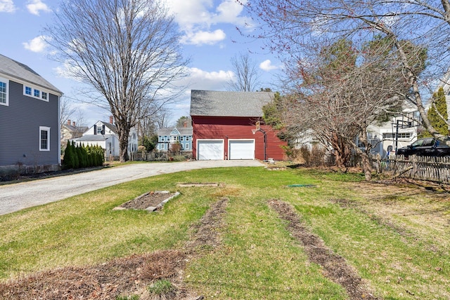 view of yard featuring a residential view, driveway, fence, a garage, and an outdoor structure