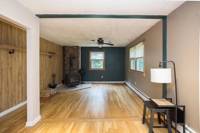 23 Orr St, Wilton, ME 04294 - unfurnished living room with a wood stove, ceiling fan, light wood-style floors, and wooden walls