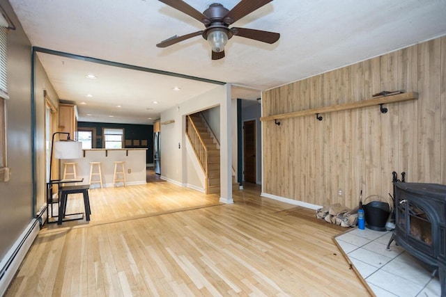 23 Orr St, Wilton, ME 04294 - unfurnished living room featuring a wood stove, baseboard heating, wood walls, light wood finished floors, and stairway