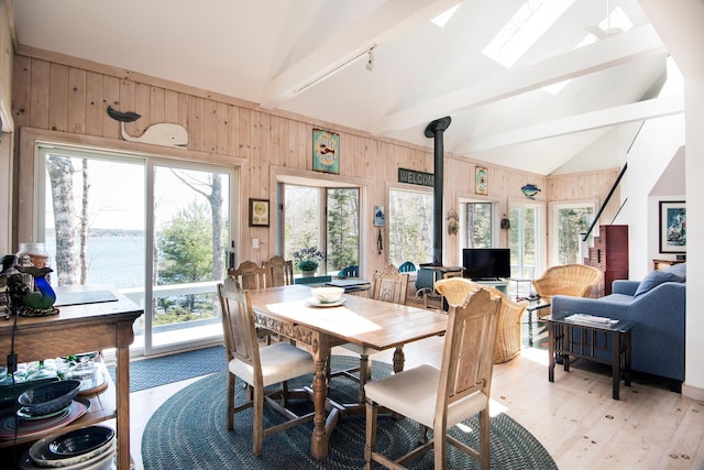 dining room with beamed ceiling, wood walls, a healthy amount of sunlight, and light wood-style flooring