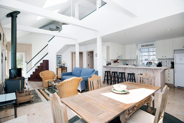 dining space with a wood stove, stairway, vaulted ceiling with beams, recessed lighting, and light wood-style flooring