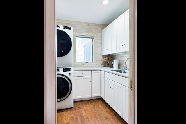 laundry room featuring cabinet space, a sink, light wood finished floors, stacked washer and clothes dryer, and recessed lighting