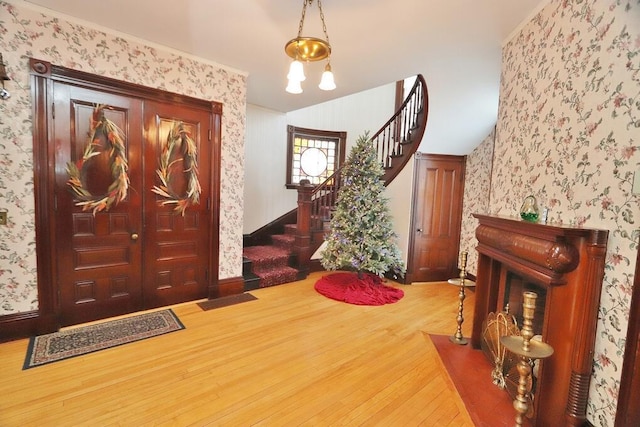foyer with stairs, wood finished floors, and wallpapered walls