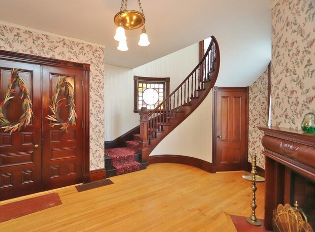 foyer entrance with wallpapered walls, baseboards, wood finished floors, and stairs