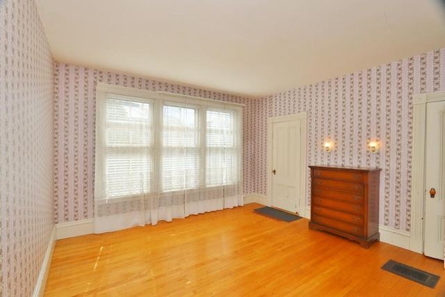unfurnished bedroom with wallpapered walls, wood finished floors, visible vents, and baseboards