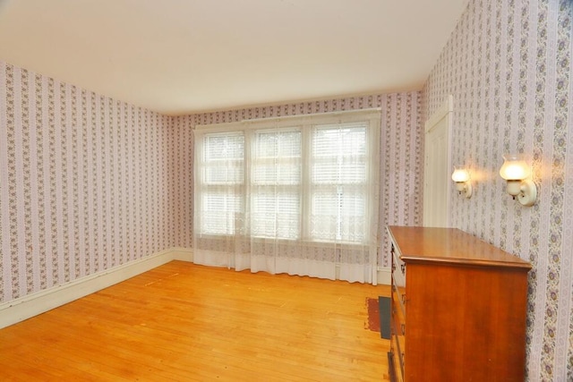 unfurnished room featuring baseboards, wallpapered walls, and light wood-type flooring