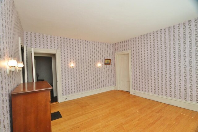 spare room featuring wallpapered walls, light wood finished floors, and baseboards
