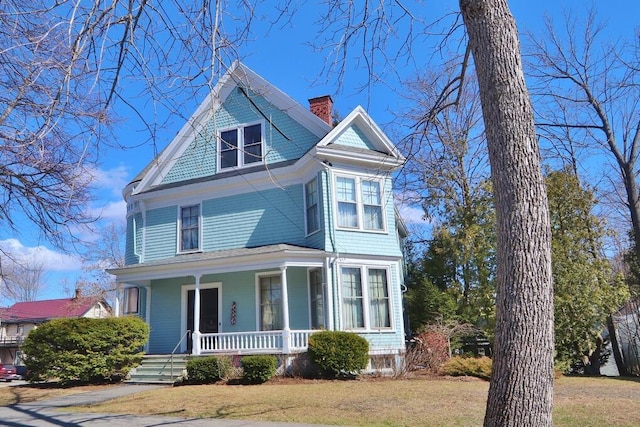 victorian home with a front lawn, a chimney, and covered porch