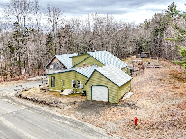 view of side of home featuring central AC unit, a garage, metal roof, and an outbuilding