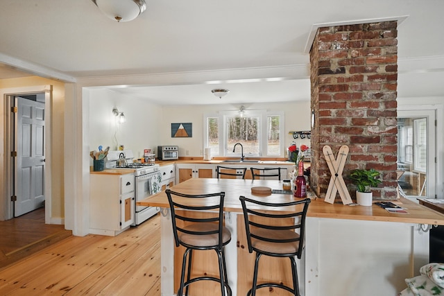 kitchen with butcher block countertops, plenty of natural light, a sink, gas range gas stove, and light wood-type flooring