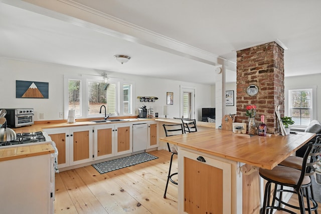 kitchen featuring dishwasher, a breakfast bar, butcher block counters, a sink, and light wood-type flooring