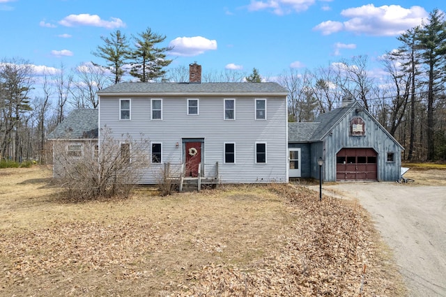 colonial inspired home with a shingled roof, a chimney, a detached garage, and dirt driveway