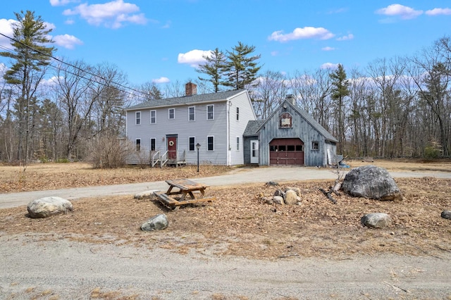 colonial-style house featuring a detached garage, driveway, and a chimney