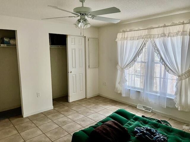 bedroom with visible vents, light tile patterned floors, baseboards, two closets, and ornamental molding