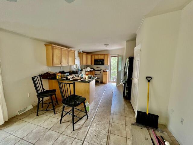 kitchen with light tile patterned flooring, dark countertops, black microwave, a peninsula, and visible vents