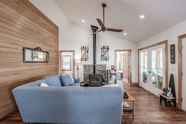 living room featuring ceiling fan, french doors, a wood stove, and wooden walls
