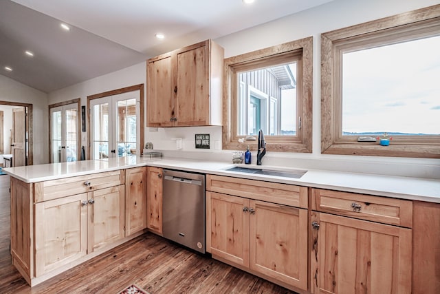 kitchen with a peninsula, stainless steel dishwasher, light brown cabinetry, a sink, and vaulted ceiling